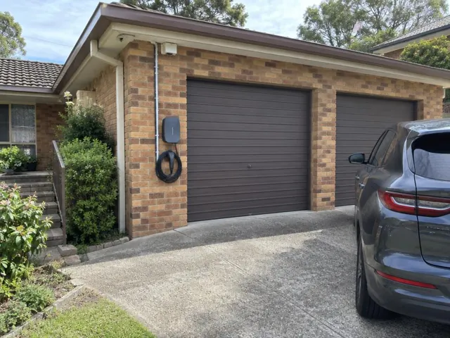 Wall-mounted EV charger on a brick garage wall beside a driveway in North Rocks