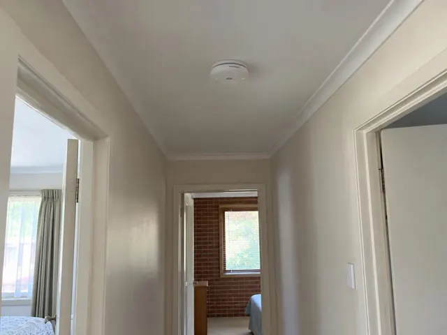 Ceiling smoke alarm in a narrow hallway with white walls and doors in Northmead